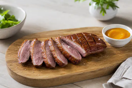 Andebryst i skiver med rosa kjøtt og sprøtt, rutet skinn på et skjærebrett med appelsinsaus ved siden av
