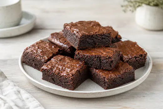 Firkantede brownies med blank sprukket overflate og kladdete midte, stablet på en tallerken