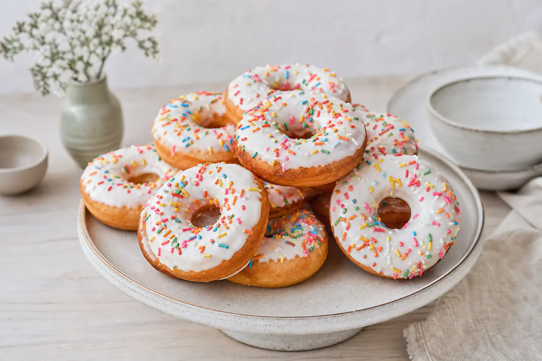 Gyllenbrune donuts med hvit glasur og fargerikt strøssel på et kakefat