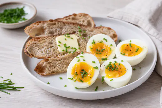 Kokte egg delt i to med gul og smilende plomme på en tallerken med brødskiver og gressløk