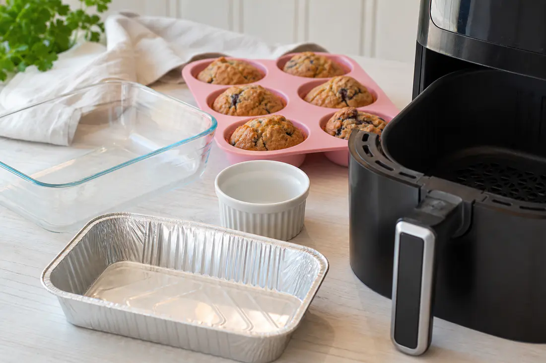 Aluminiumsform, ovnfast glassform, keramisk ramekin og silikonform med muffins ved siden av en airfryerkurv
