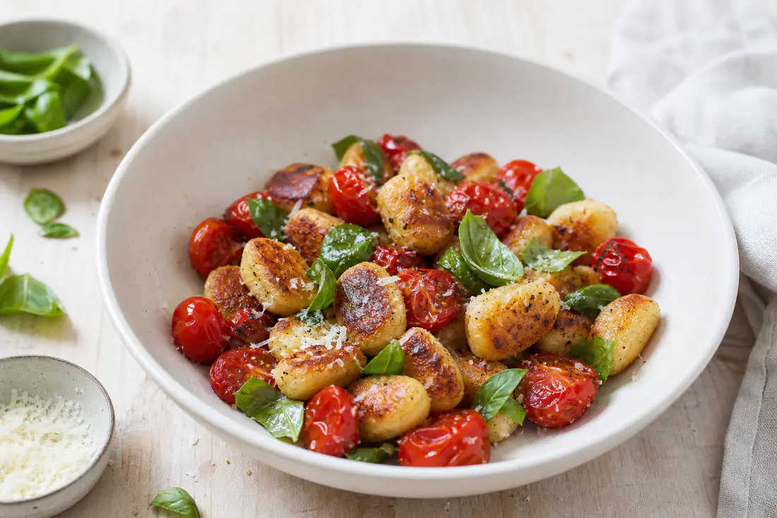 Gyldne, sprø gnocchi med blistrede cherrytomater, revet parmesan og basilikum i en dyp tallerken