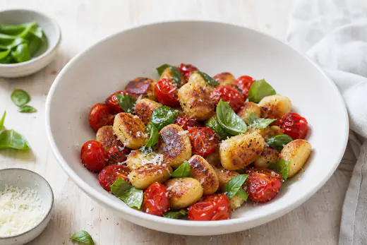 Gyldne, sprø gnocchi med blistrede cherrytomater, revet parmesan og basilikum i en dyp tallerken