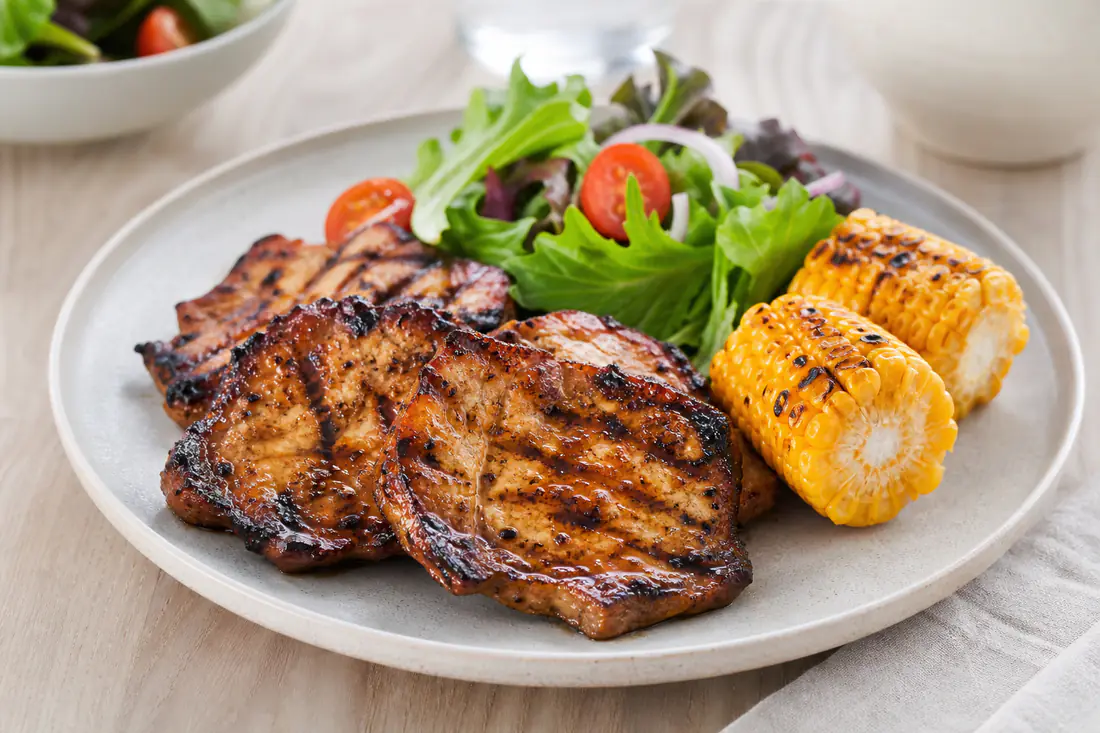 Stekte, tynne grillskiver av svin med mørke grillstriper og marinade, servert med salat og poteter