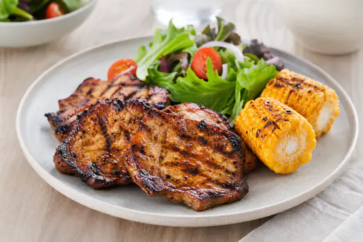 Stekte, tynne grillskiver av svin med mørke grillstriper og marinade, servert med salat og poteter