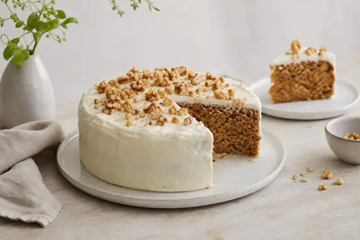 Gulrotkake med hvit kremostfrosting og hakkede valnøtter på toppen, en skive tatt ut på en tallerken