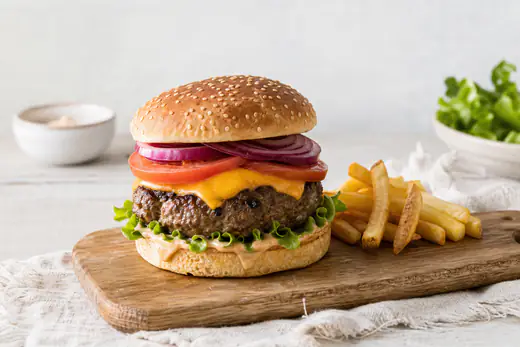 Hamburger med saftig burgerpatty, smeltet ost, salat og tomat i et hamburgerbrød på et trebrett