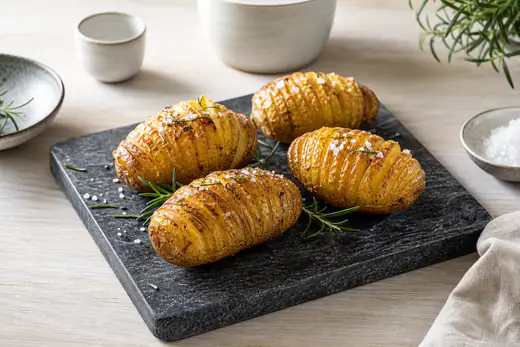 Fire gyllne hasselbackpoteter med sprø, vifteformede skiver og rosmarin på et steinbrett