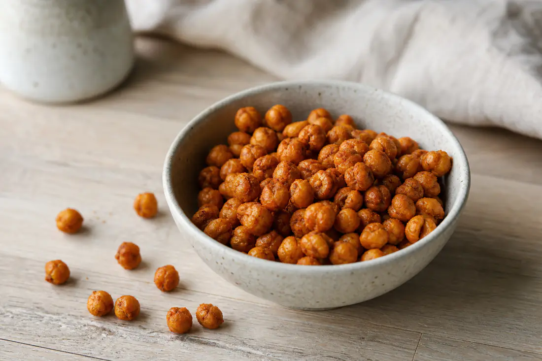 Sprø ristede kikerter med paprika i en liten skål, med noen kikerter strødd utover bordet