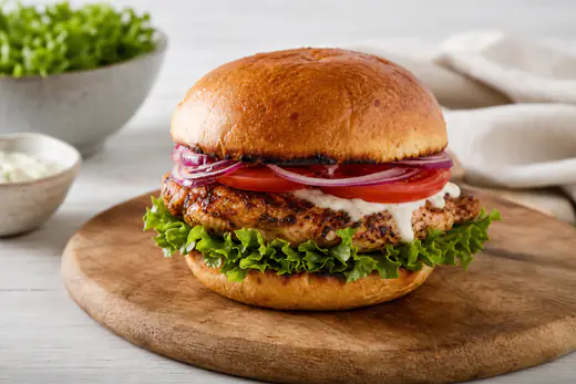 Kyllingburger i ristet hamburgerbrød med salat, tomat, rødløk og hvit dressing på et trebrett