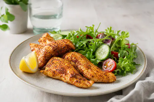 Paprikakrydret kyllinginnerfilet med gyllen overflate på en tallerken med salat og sitronbåt