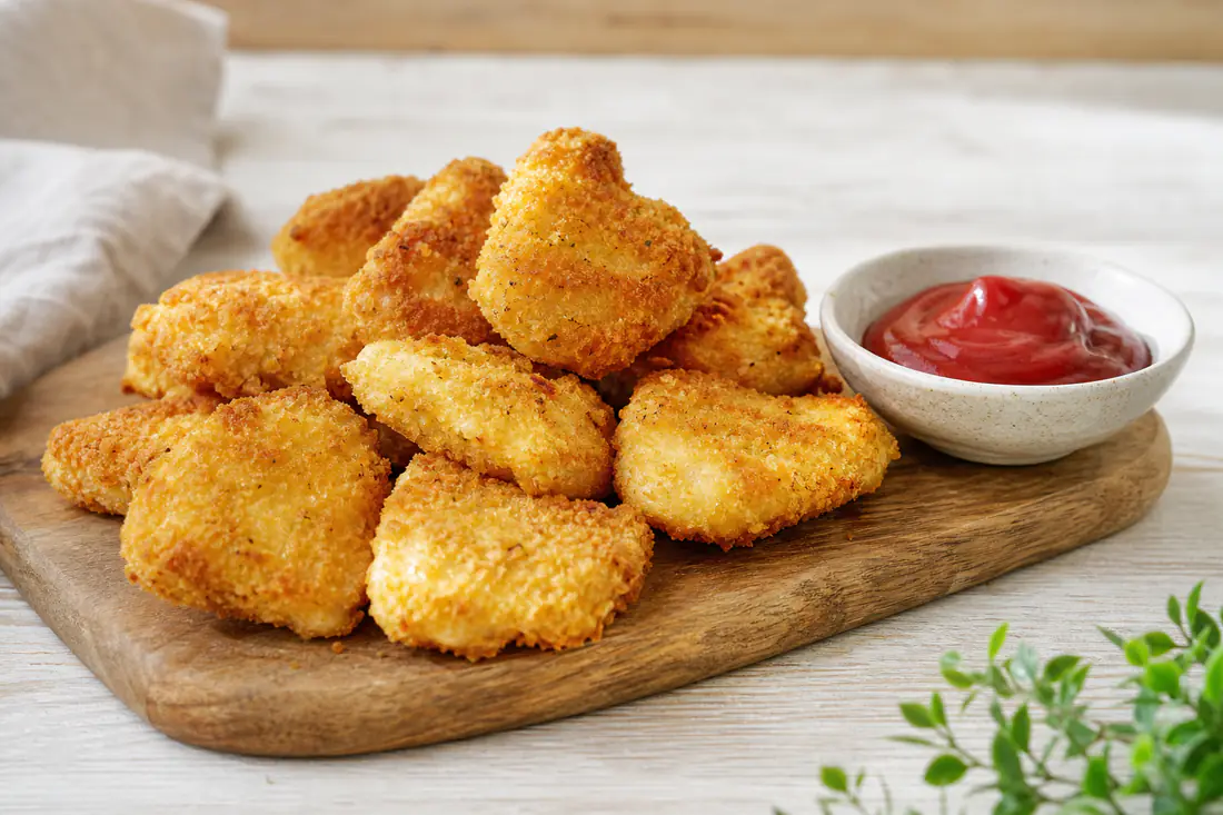 Gyllne, hjemmelagde kyllingnuggets på et trebrett med en liten skål ketchup