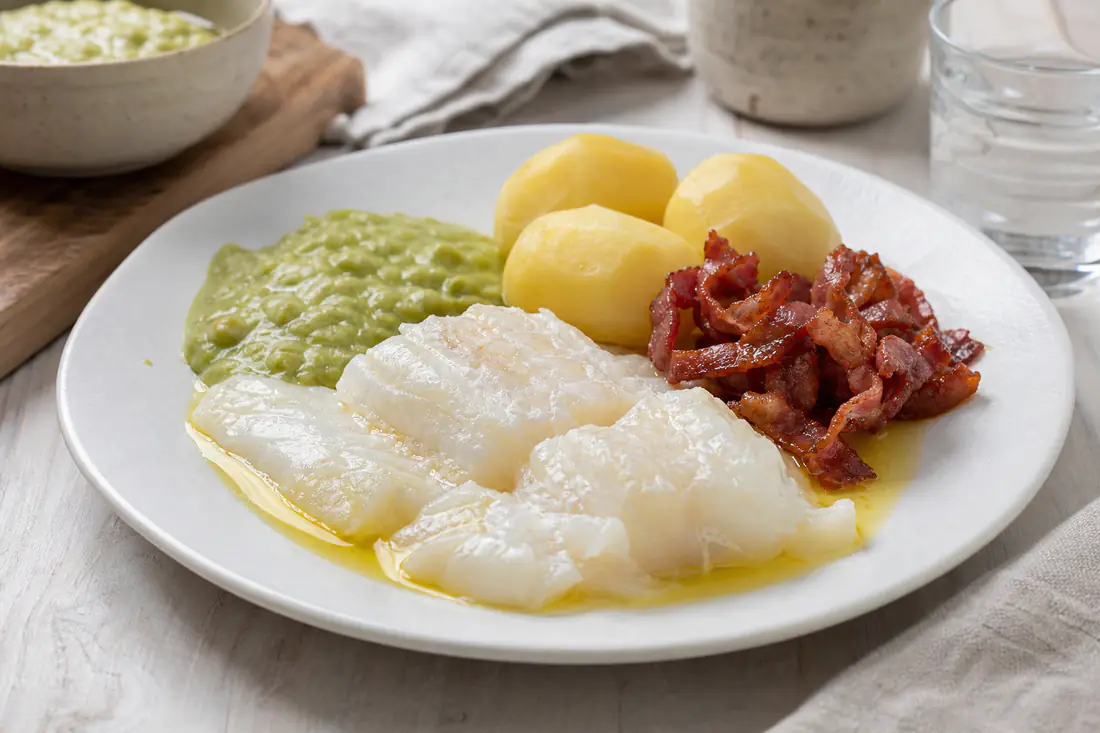 Lutefisk i en ildfast form med bacon, kokte poteter, ertestuing og smeltet smør