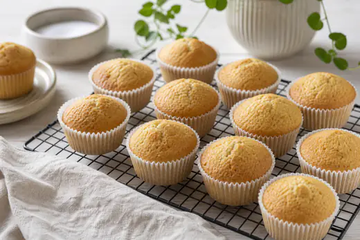 Gylne vaniljemuffins i papirformer på en rist på et lyst kjøkkenbord