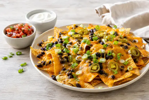 Nachos med smeltet cheddar, svarte bønner, jalapeños og vårløk på et fat med salsa og rømme