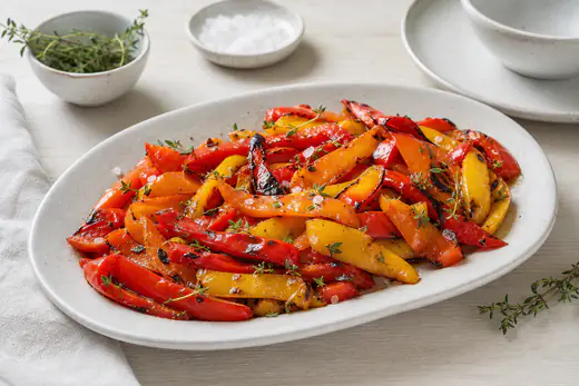 Grillede strimler av rød, gul og oransje paprika med svidde kanter på et fat med flaksalt og timian