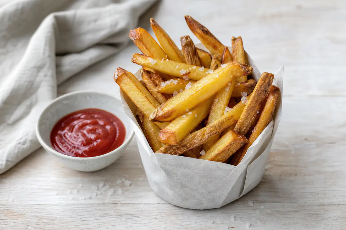 Gylne hjemmelagde pommes frites med flaksalt i en papirbeholder med en skål ketchup ved siden av