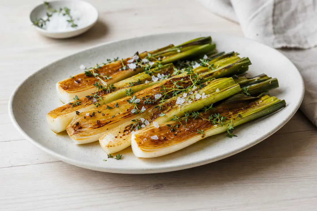 Halverte purreløk med gylne, karamelliserte snittflater på et fat med timian og flaksalt