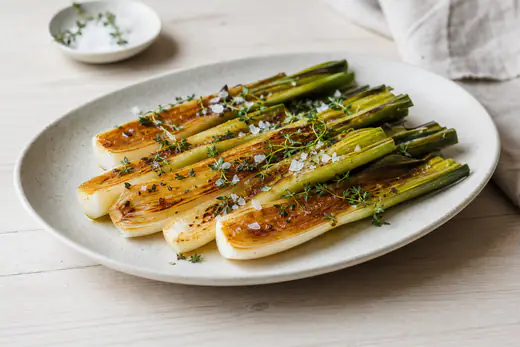 Halverte purreløk med gylne, karamelliserte snittflater på et fat med timian og flaksalt