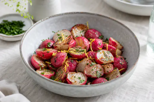 Halverte ristede reddiker med brune snittflater, persille og sitronskall i en grå steintøyskål