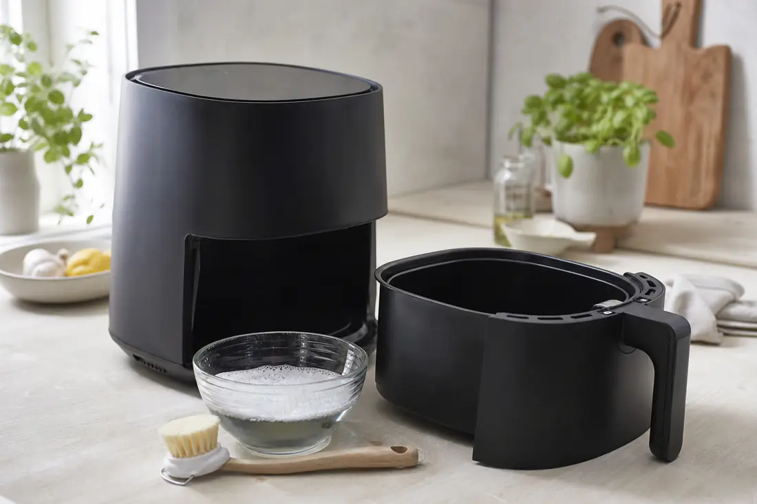 Ren airfryer med uttrukket kurv ved siden av en oppvaskbørste og en bolle med såpevann