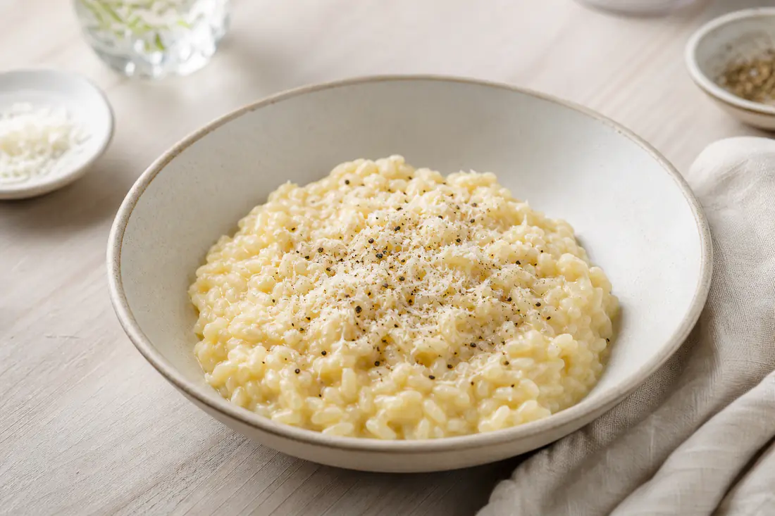 Kremet parmesanrisotto i en dyp tallerken, toppet med revet parmesan og nykvernet pepper