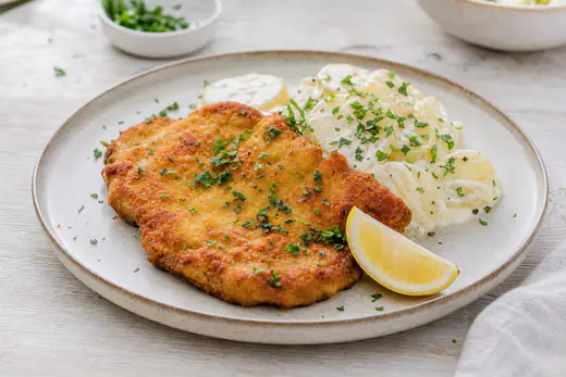 Gyllen panert svineschnitzel på en tallerken med sitronbåt, potetsalat og et dryss persille