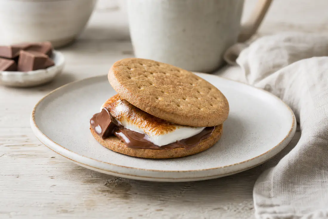 S'mores med gylne ristede marshmallows og smeltet sjokolade mellom to kjeks, på en tallerken