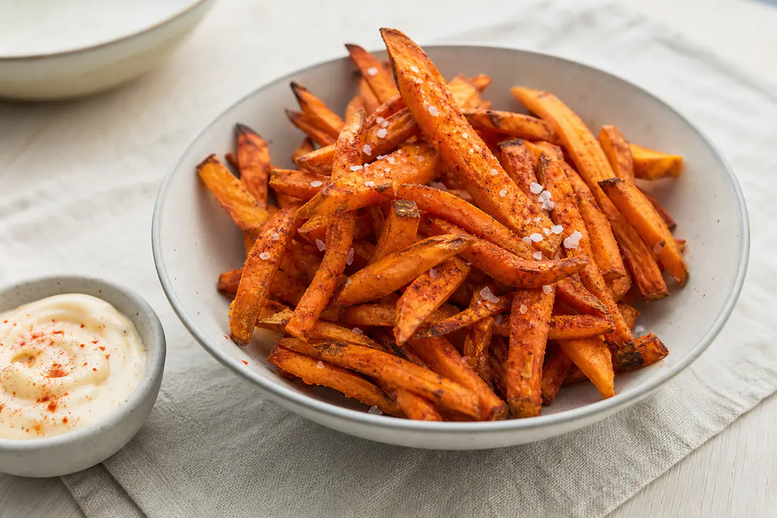 Oransje søtpotetfries med paprika og flaksalt i en skål med en liten skål aioli ved siden av