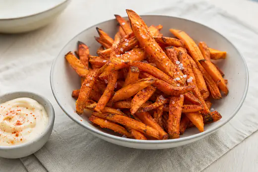 Oransje søtpotetfries med paprika og flaksalt i en skål med en liten skål aioli ved siden av
