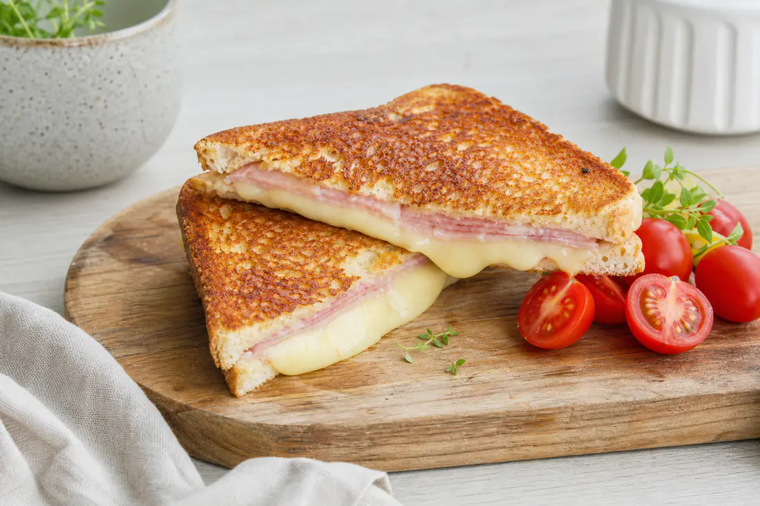 Gyllen toast med skinke og smeltet ost delt diagonalt på et skjærebrett med cherrytomater