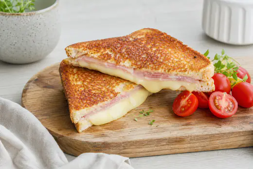 Gyllen toast med skinke og smeltet ost delt diagonalt på et skjærebrett med cherrytomater